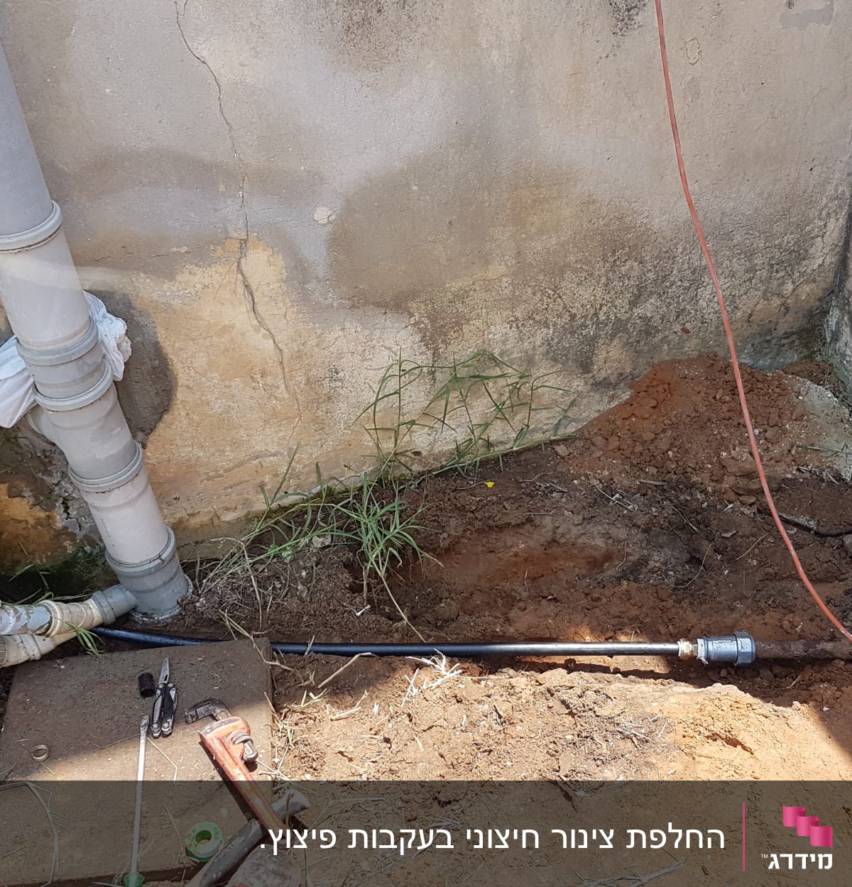 צינורות מים וכלי עבודה על הקרקע ליד קיר